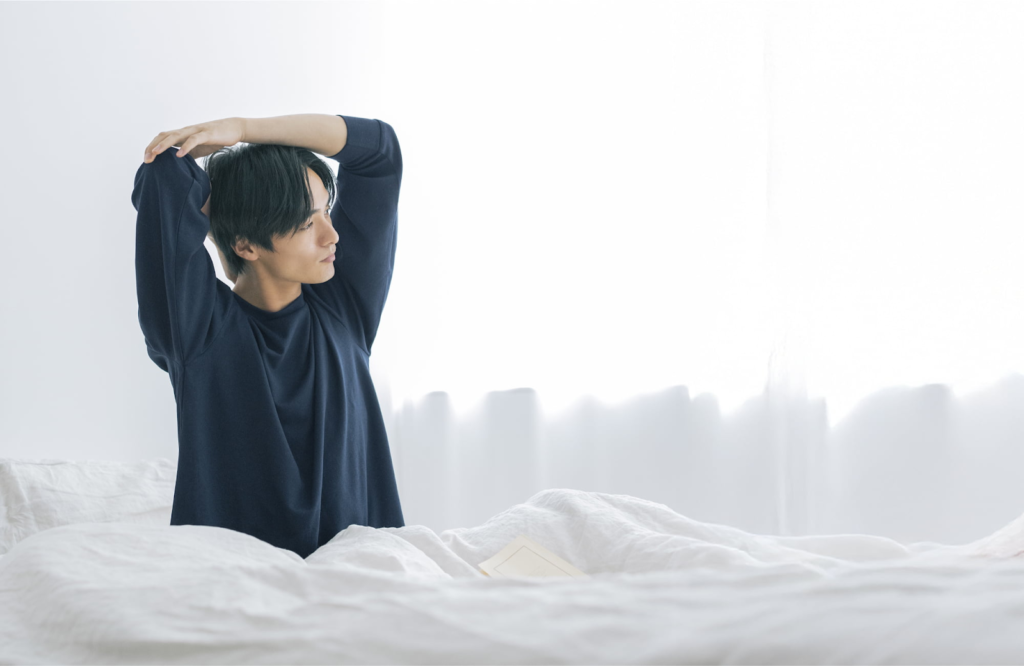 Recoverypro Lab.のリカバリーウェアを着用した男性が朝ベッドで伸びをしている様子